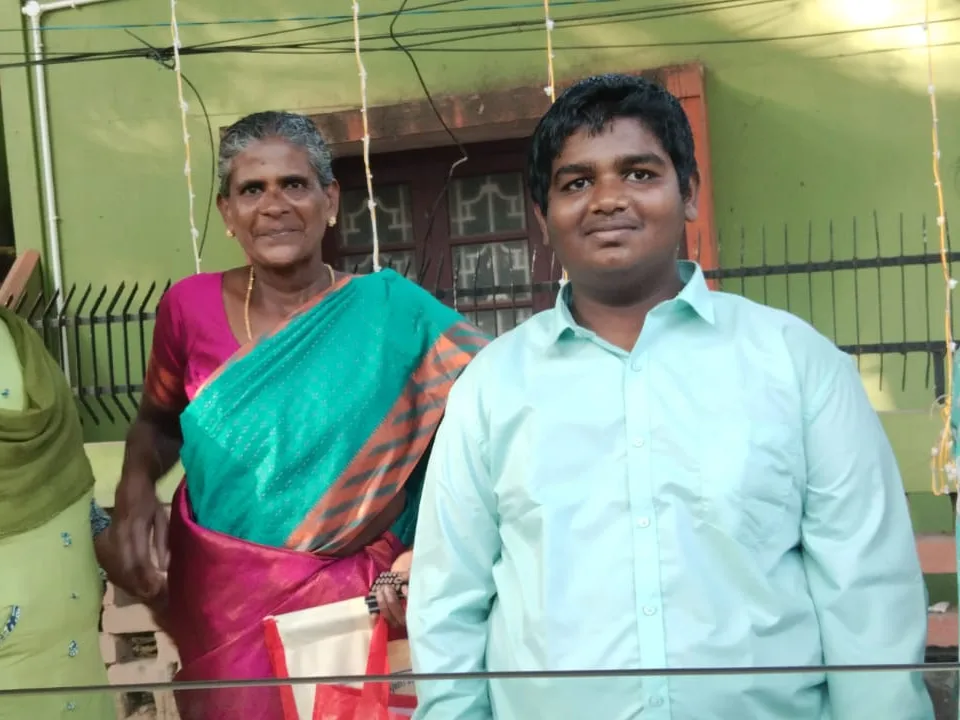 A boy standing beside an older woman outdoors, in front of a house