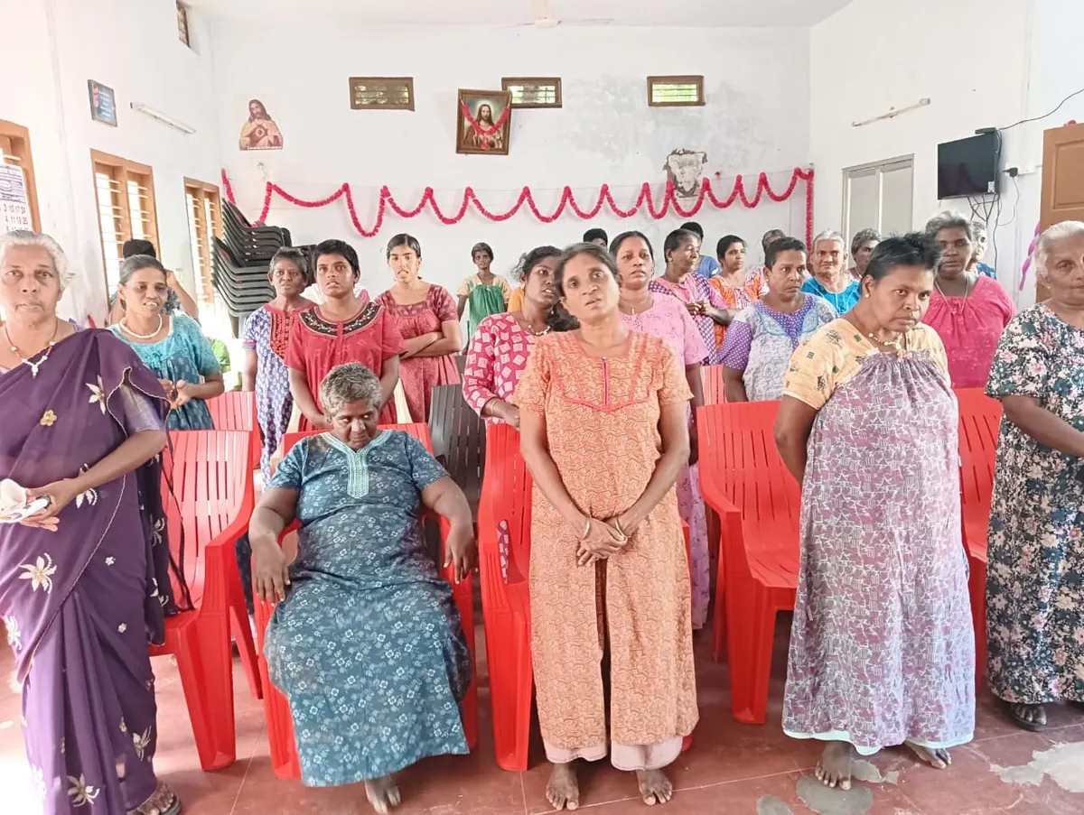 Women standing and seated together in a hall, wearing matching dresses