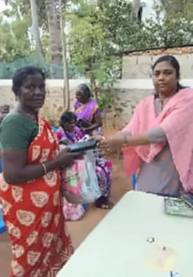 A woman in a pink shawl with a woman in a red saree, who is holding a bag, in front of a table