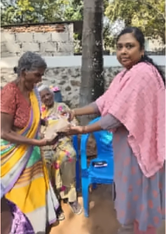 A woman in a pink shawl with an older woman in a yellow and green saree, with a seated woman behind them