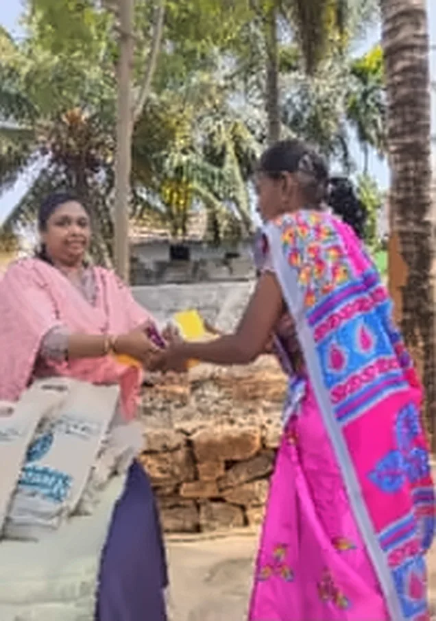 A woman in a pink shawl handing a gift to a woman in a bright pink saree