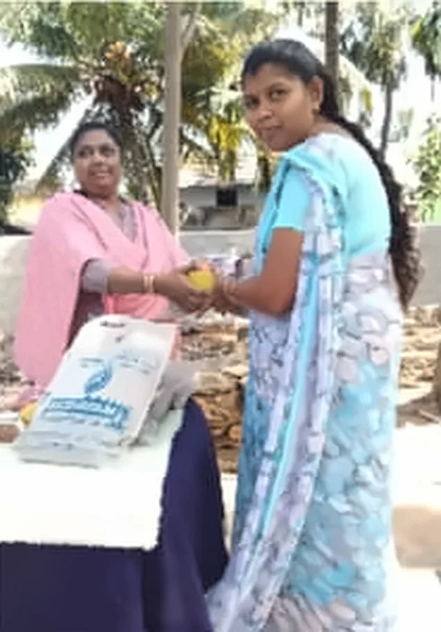 A woman in a pink shawl handing a gift to a young woman in a light blue saree