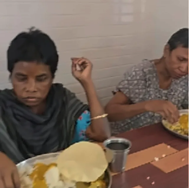Two women sitting at a table, eating a meal of rice, curry and a papad