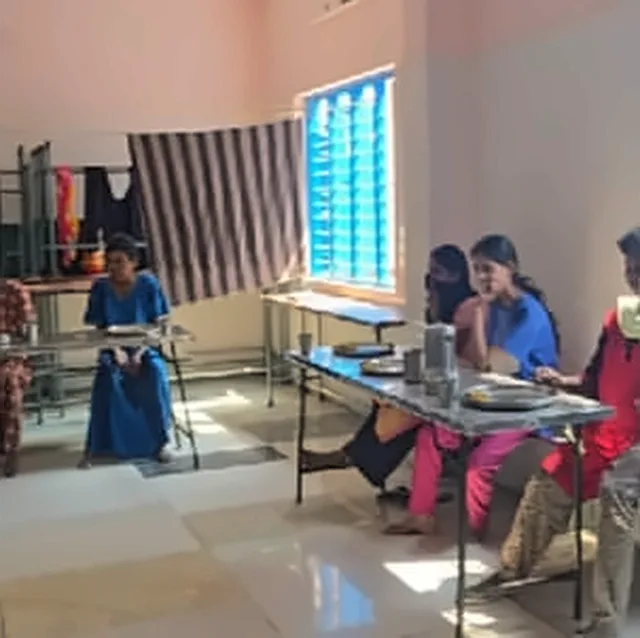 Women and children seated at tables in a dining room with a window with blue shutters
