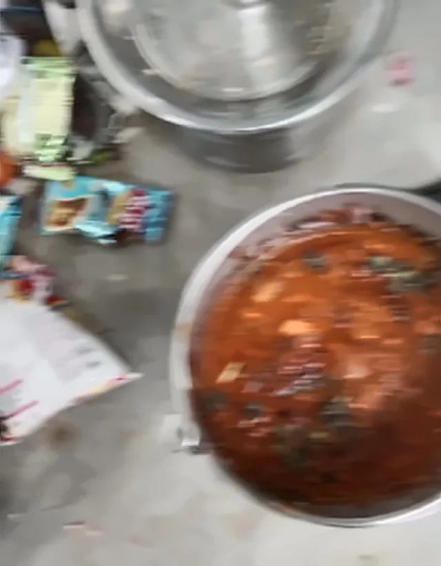 A steel pot of curry on a floor, with packets of snacks beside it