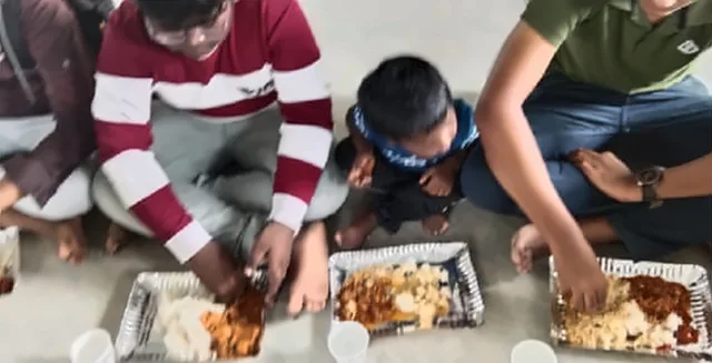 Boys and young men sitting on the floor eating from foil trays