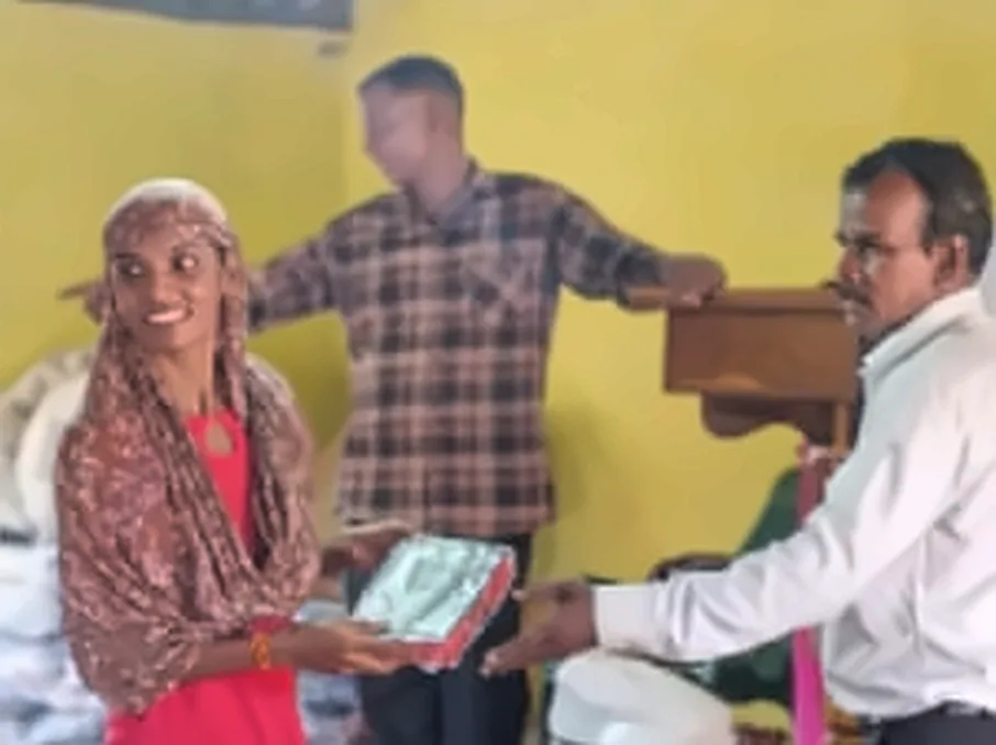 A smiling woman receiving a Bible from a man in a white shirt, in a hall with yellow walls