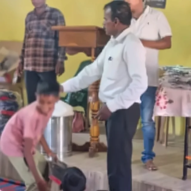 A boy in a pink shirt and a man in a white shirt handing out Bibles at a wooden stand