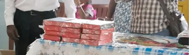 Stacks of Bibles wrapped in red and silver packaging on a table, with people standing behind
