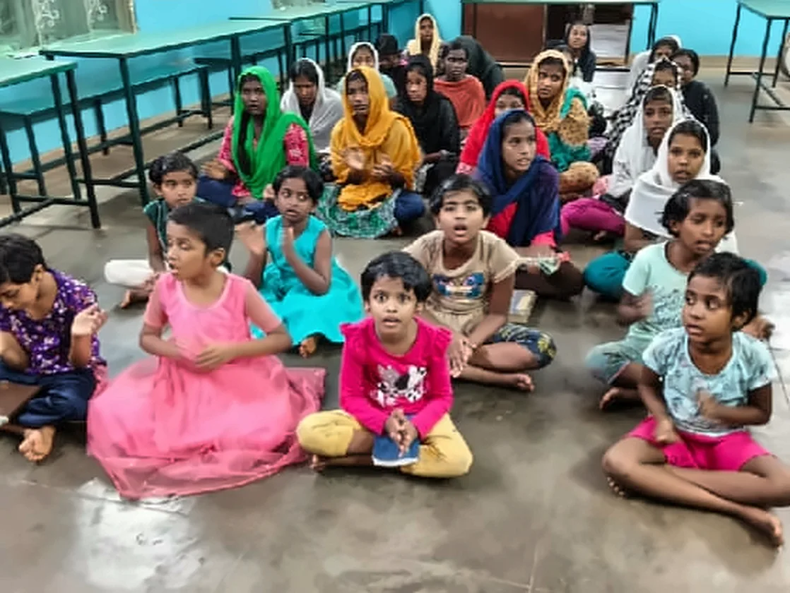 Girls and young children sitting together on the floor of a hall