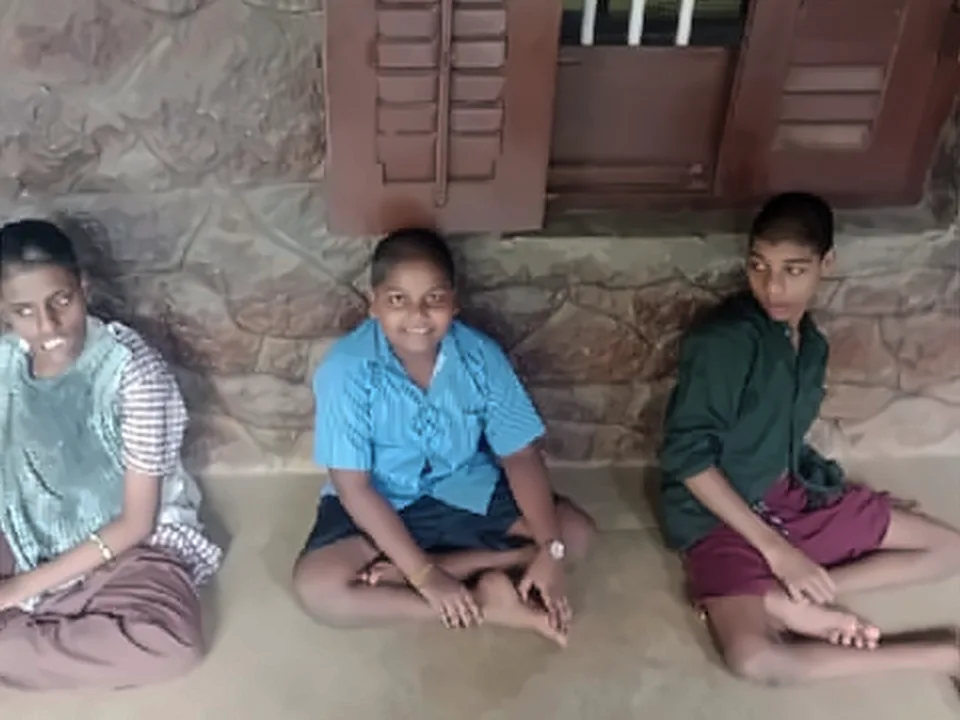 Three young people sitting on the floor in front of a stone wall