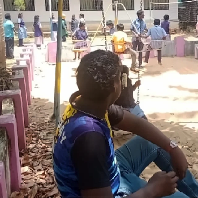 A boy in a blue and black top sitting at a playground, with a swing and other children behind him