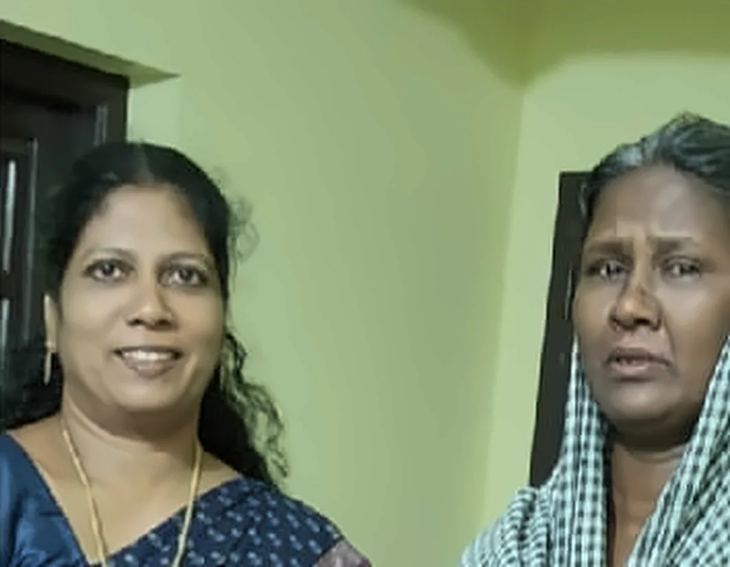 A woman in a blue saree standing with a woman in a pink dress, who has her hands pressed together
